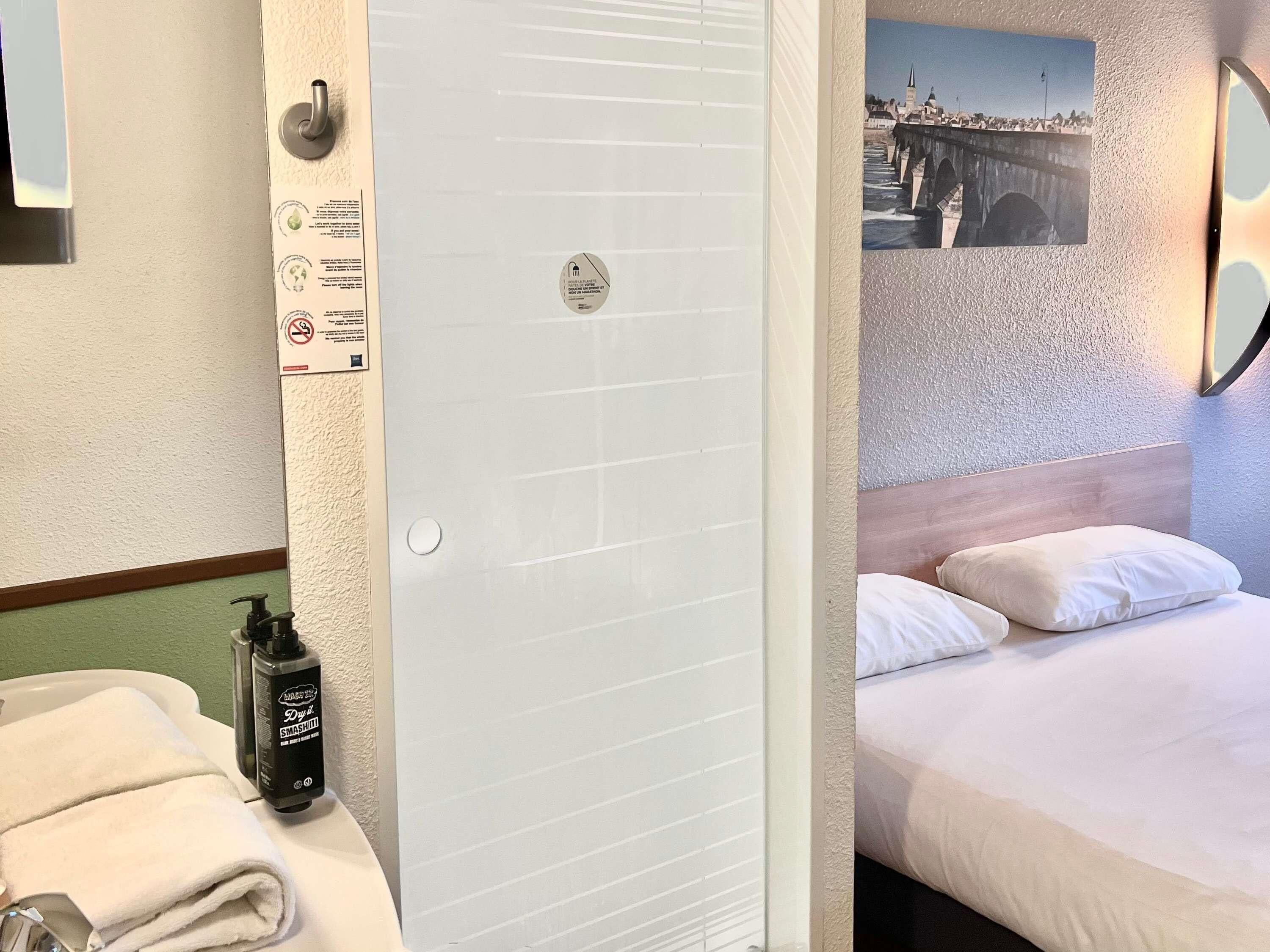 A hotel room with a bed, a bathroom with a towel and a bottle, and a picture on the wall.