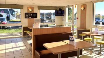 Interior de restaurante con cabinas, mesas y una pantalla de televisión.