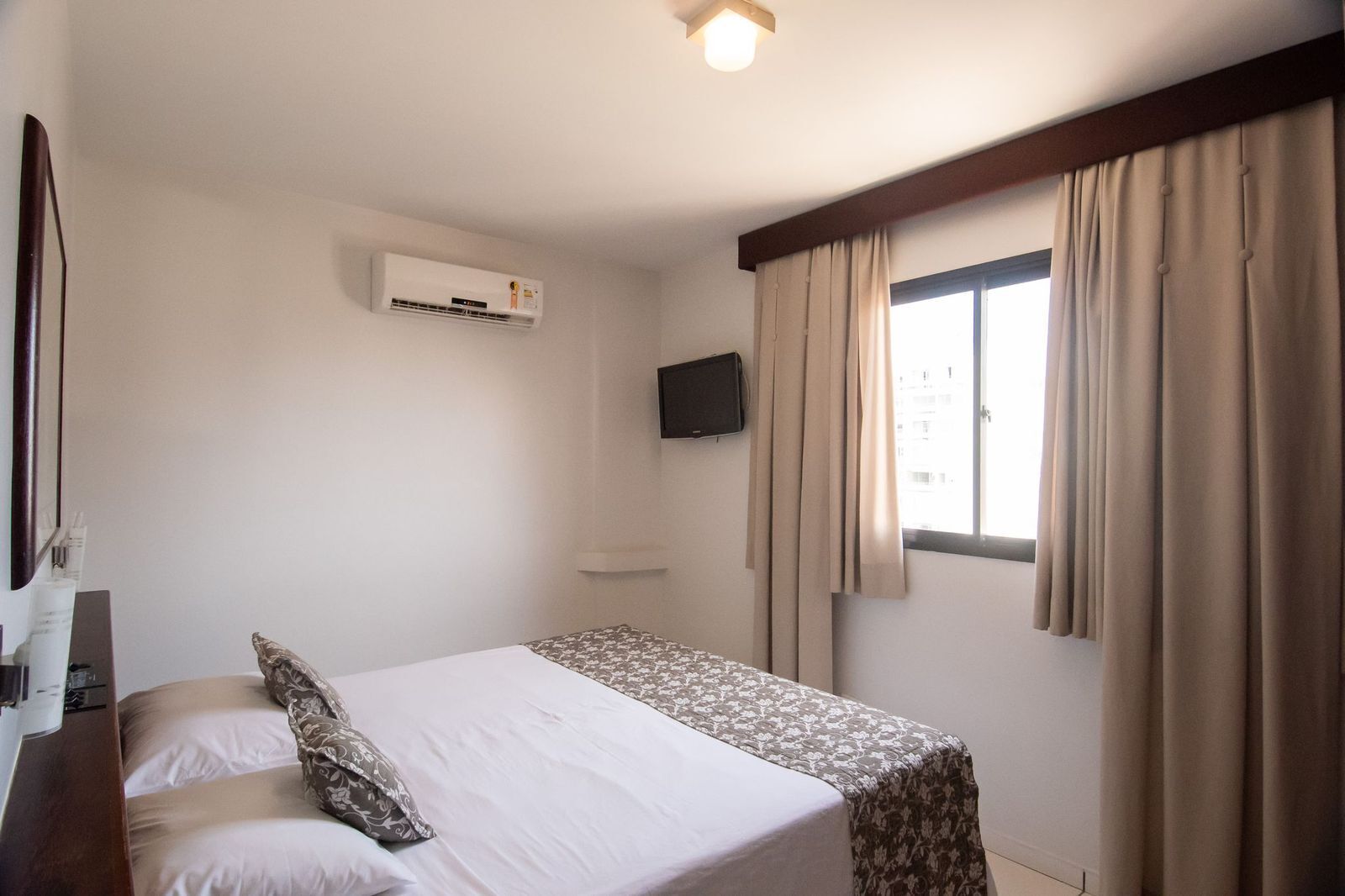 Ein Hotelzimmer mit Bett, Wandfernseher, Klimaanlage und einem fenster mit Vorhängen.
