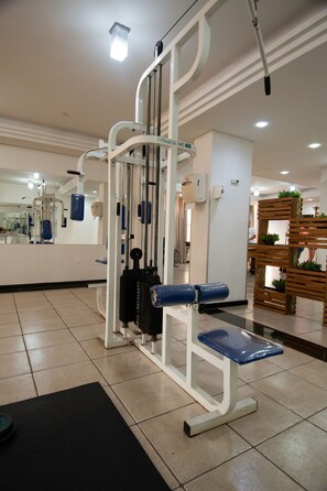 A gym with exercise equipment, a mirror, and a wooden plant display. - Golden Ingá Hotel (Maringá)