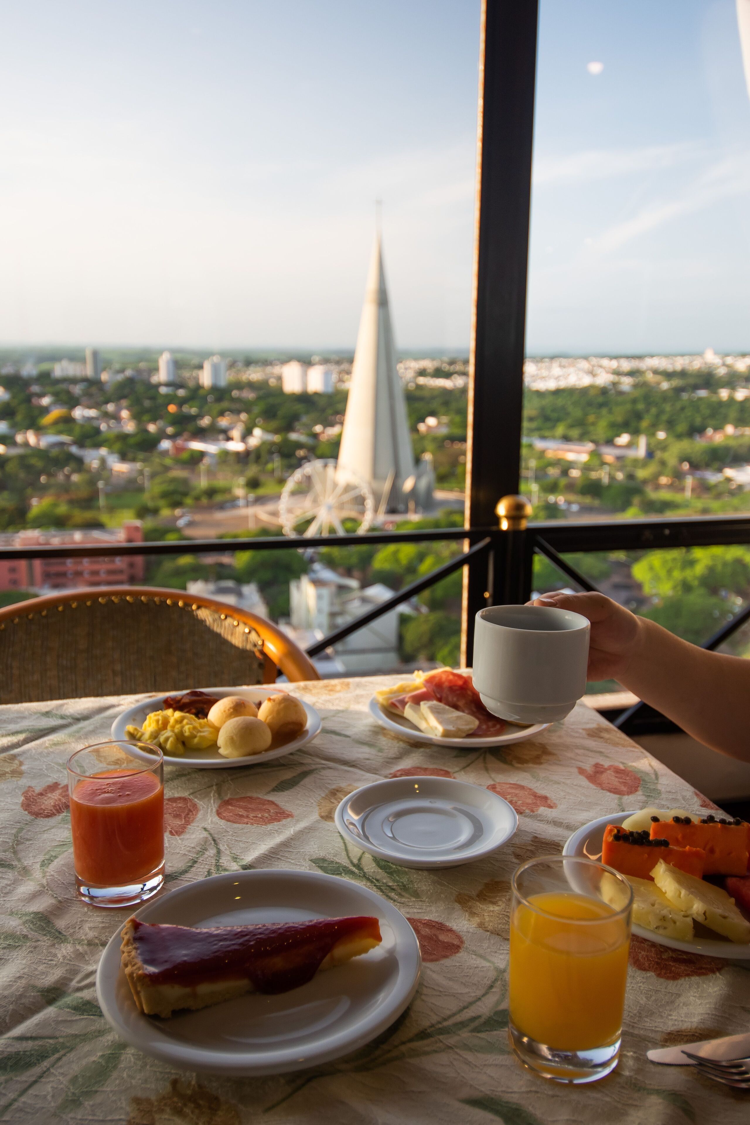 Een ontbijttafel met borden vol eten, een glas sinaasappelsap en een kop koffie, met uitzicht op een stadsbeeld met een opvallende toren en een reuzenrad.
