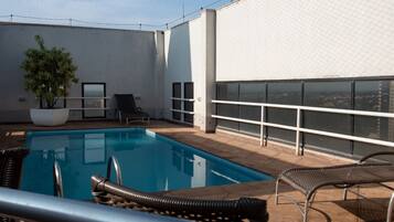 A rooftop pool area with a clear view of the city, a potted plant, and two lounge chairs.
