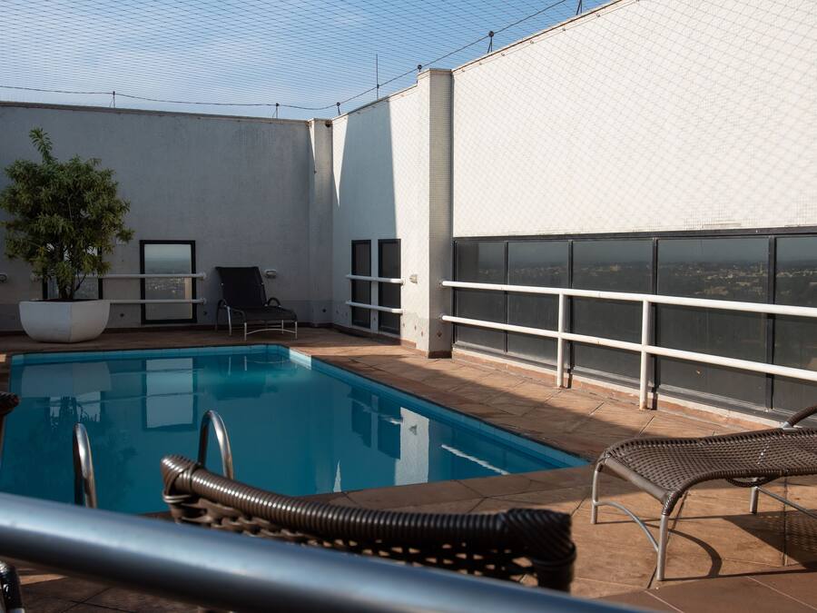 A rooftop pool area with a clear view of the city, a potted plant, and two lounge chairs.