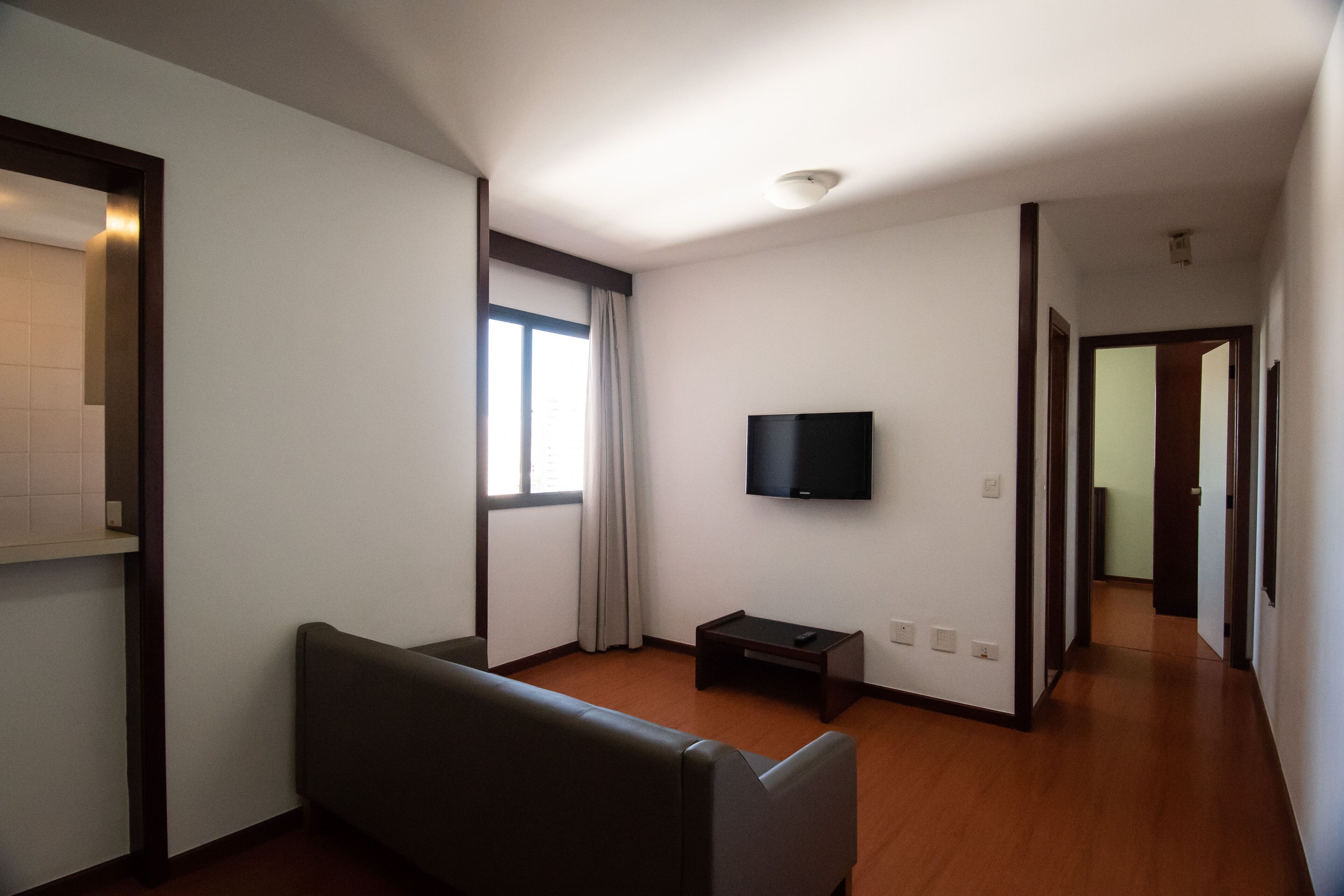 Un salón espacioso con un amplio ventanal, un televisor de pantalla plana montado en la pared y un sofá de color oscuro.
