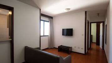Un salón espacioso con un amplio ventanal, un televisor de pantalla plana montado en la pared y un sofá de color oscuro.