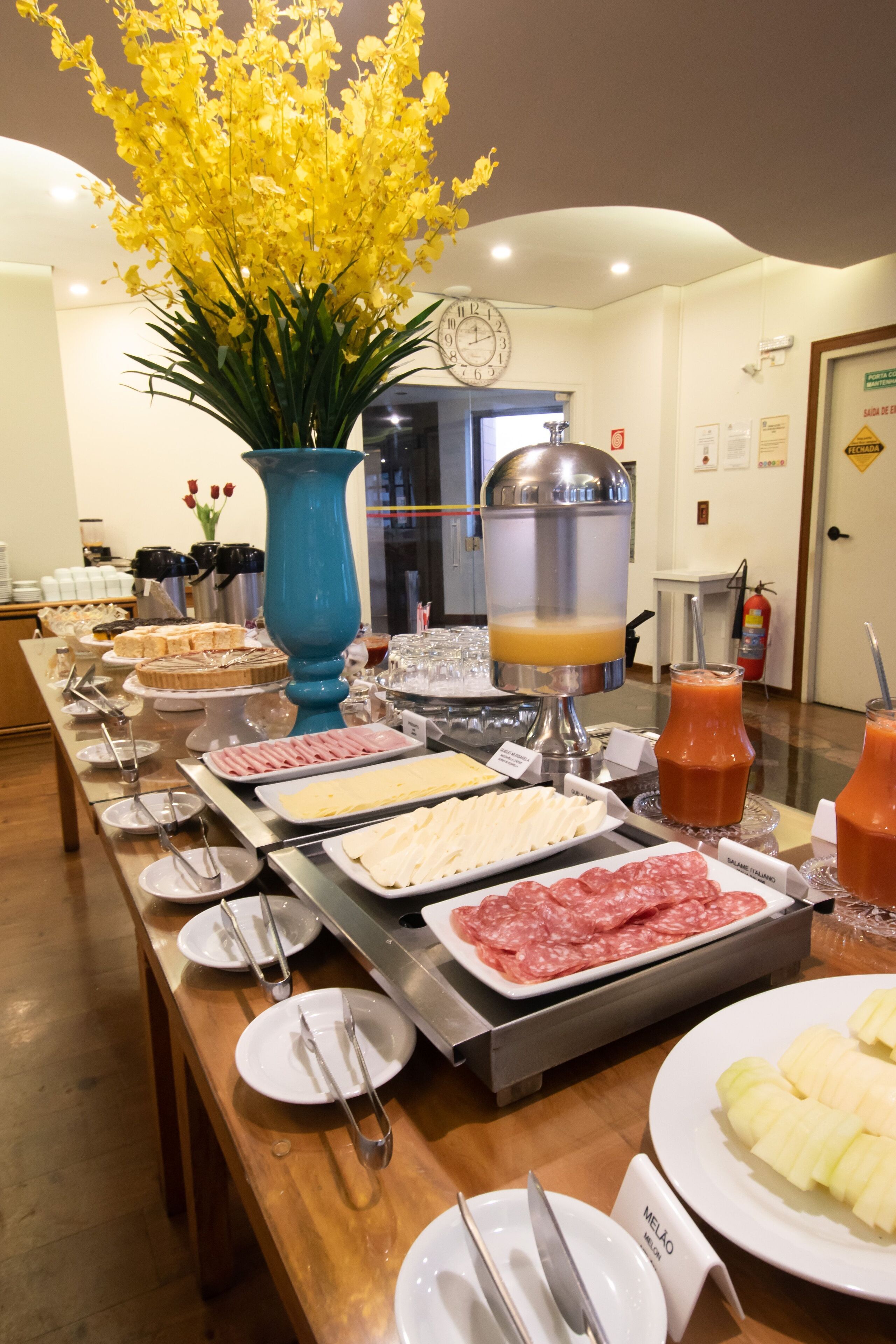 A buffet with various food items and a large vase of yellow flowers.