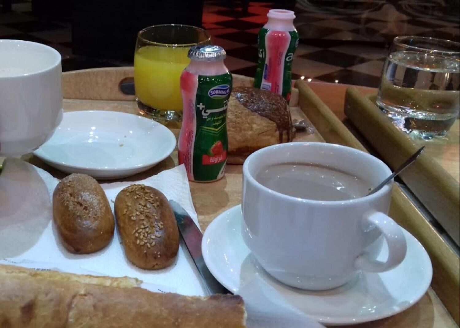 Un vassoio per la colazione con pane, una tazza di caffè, un bicchiere di succo d'arancia e una bottiglia di latte.