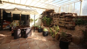 Une serre dotée d’un toit en verre, de murs en pierre et de diverses plantes en pot.