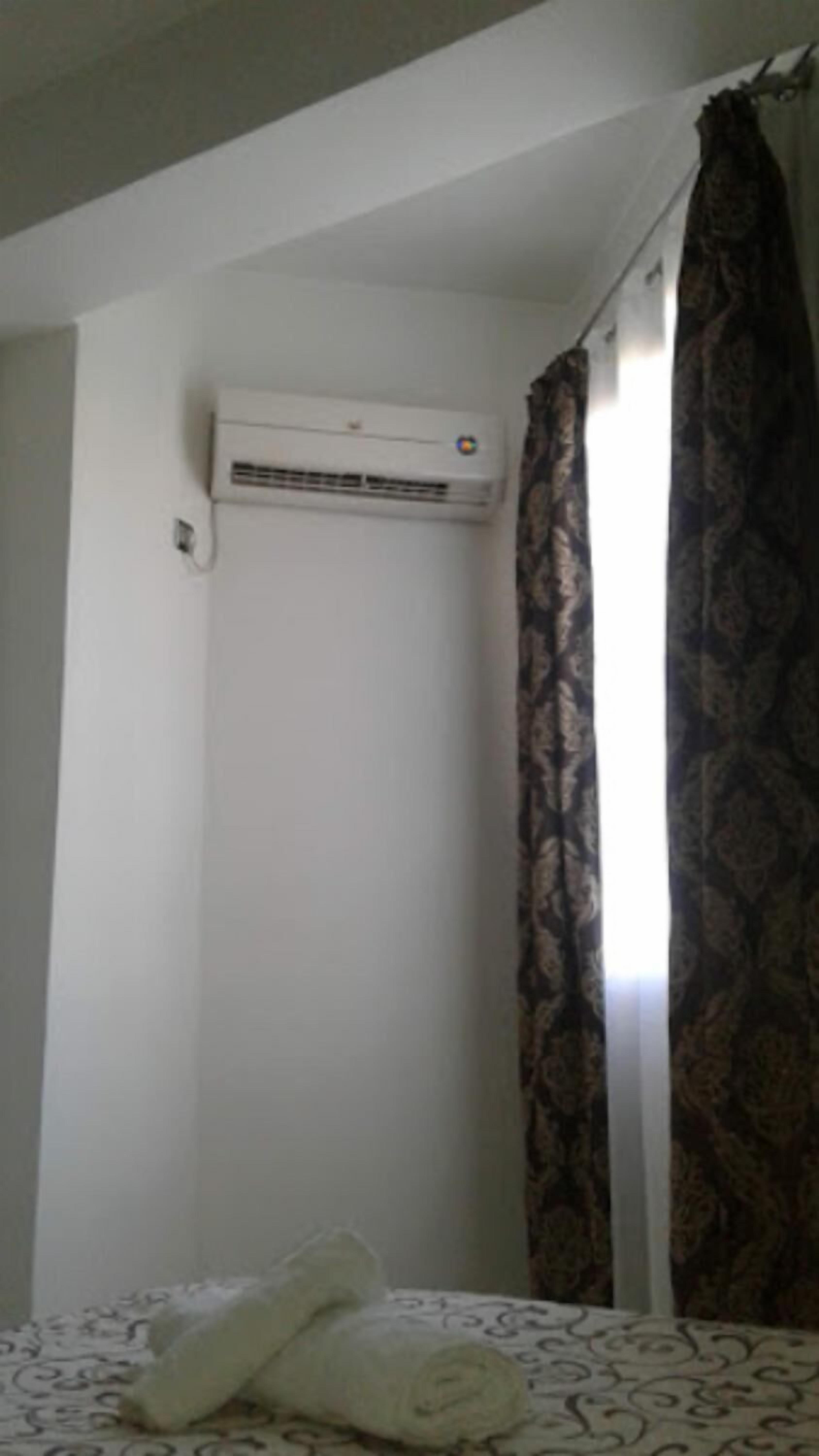 A hotel room with a bed, a patterned curtain, and an air conditioning unit on the wall.