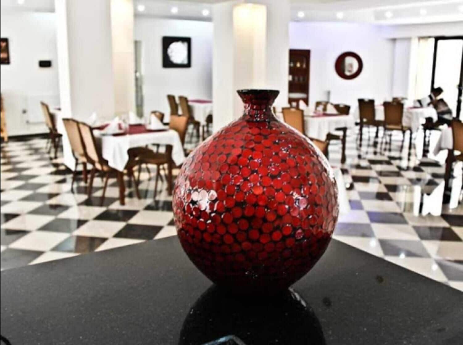 A dining area with a checkered floor, tables, chairs, and a decorative red vase.
