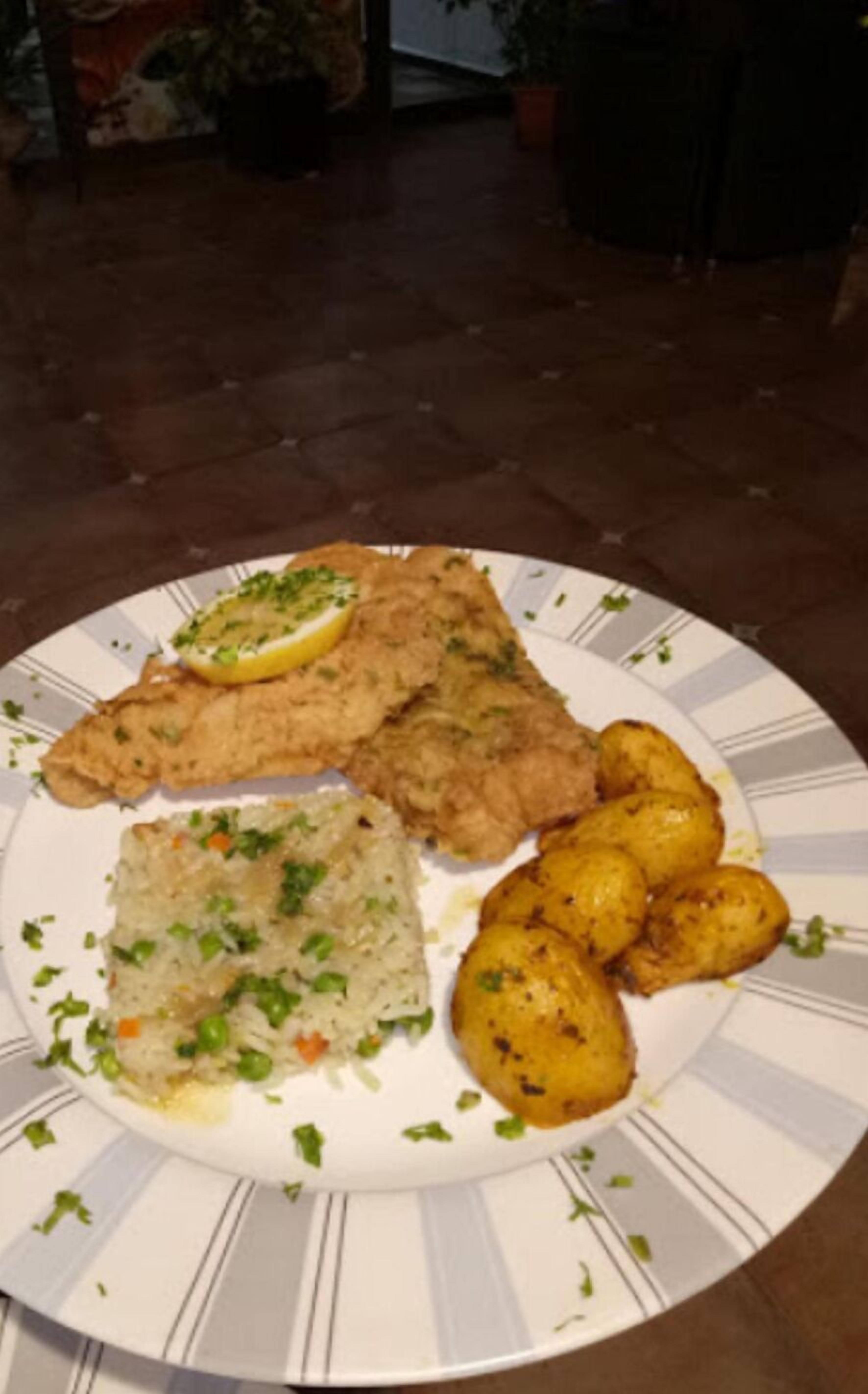 Un plato con pescado frito, arroz frito y patatas asadas.