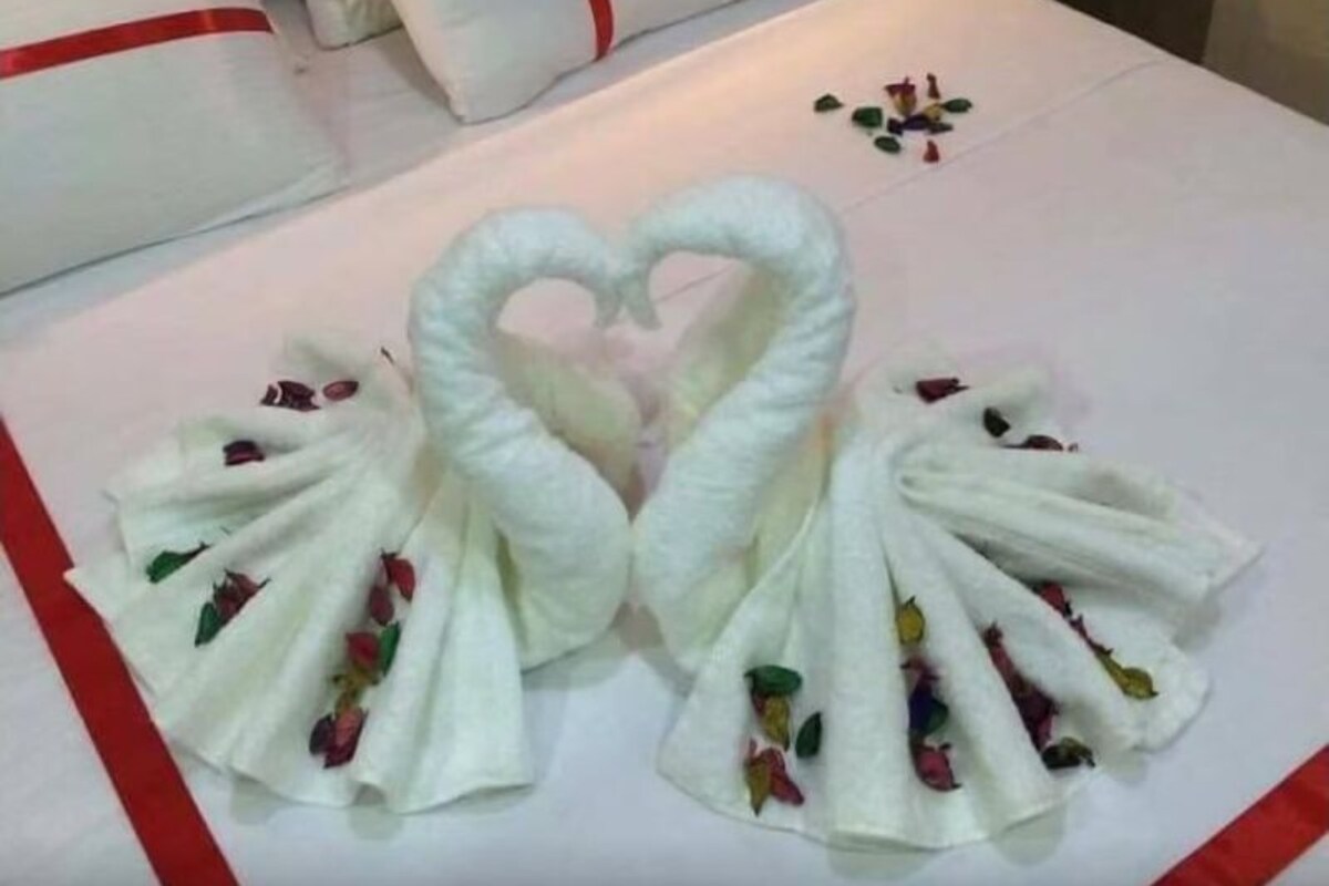 A neatly made bed with a heart-shaped towel arrangement and a pillow tied with a red ribbon.
