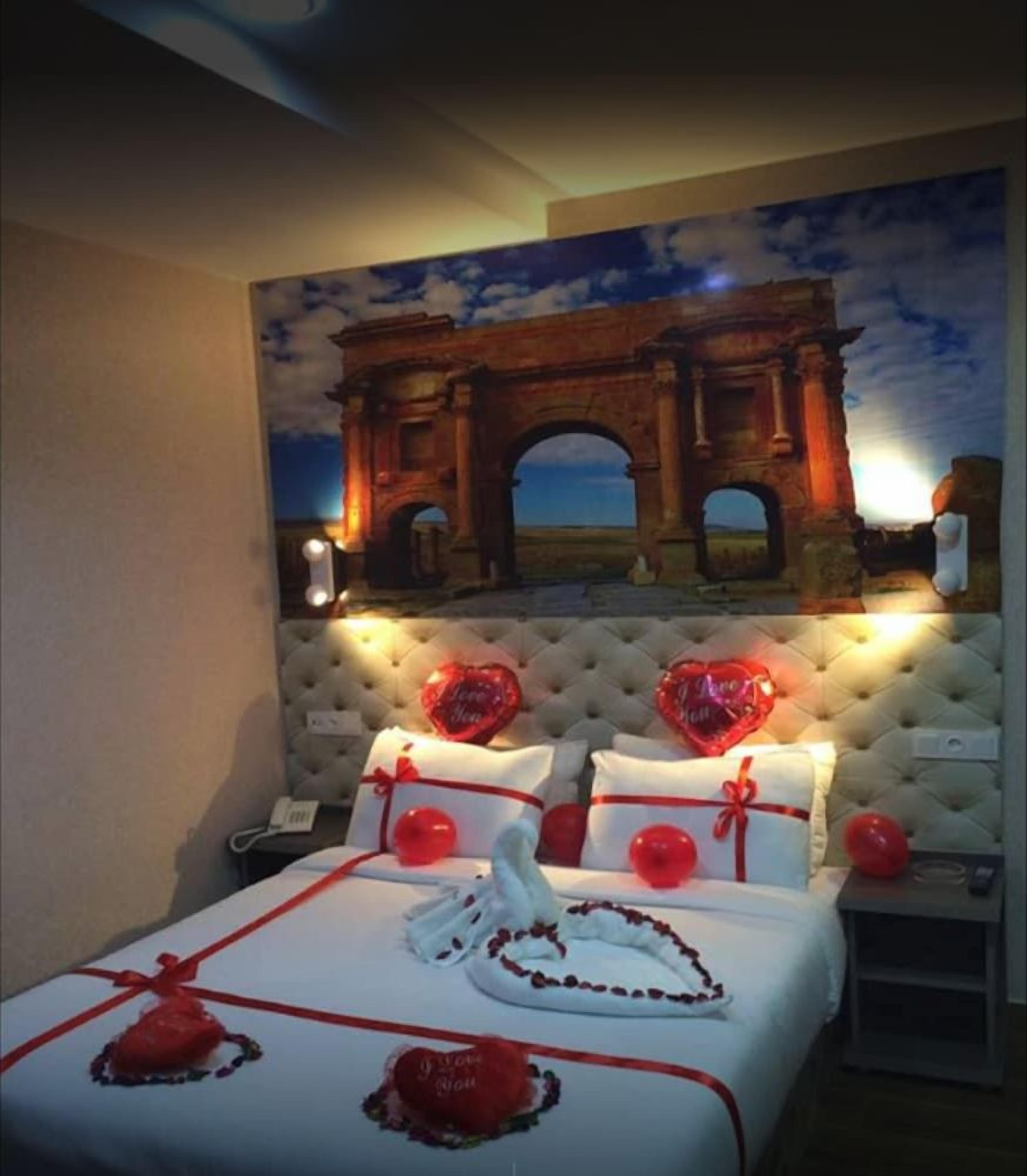 Une chambre d’hôtel avec un lit, une tête de lit capitonnée et une fresque murale représentant une arche.