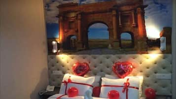 A hotel room with a bed, a tufted headboard, and a wall mural of an arch.