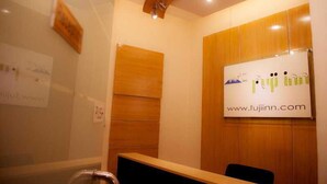 A reception area with a wooden reception desk, a whiteboard with the website 'www.fujinn.com', and a glass partition. - Fuji Inn (GULSHAN 1)