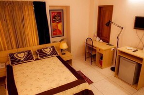A bedroom with a bed, desk, chair, lamp, and a small refrigerator. - Fuji Inn (GULSHAN 1)