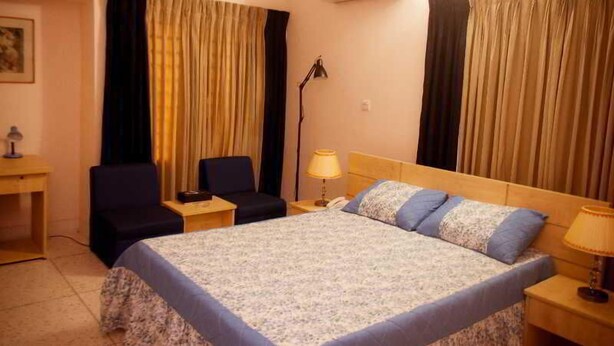 A hotel room with a bed, a desk, a chair, a lamp, and curtains. - Fuji Inn (GULSHAN 1)