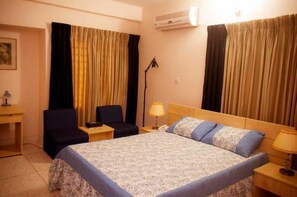 A hotel room with a bed, a desk, a chair, a lamp, and curtains. - Fuji Inn (GULSHAN 1)