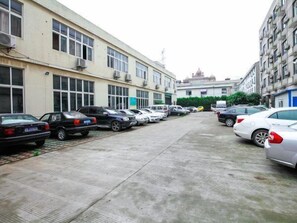 Un parking où de nombreuses voitures sont garées en rangées, à côté d’un bâtiment doté de grandes fenêtres et de climatiseurs.