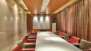 A conference room with a long table, red and beige chairs, a projector screen, and a wooden ceiling.