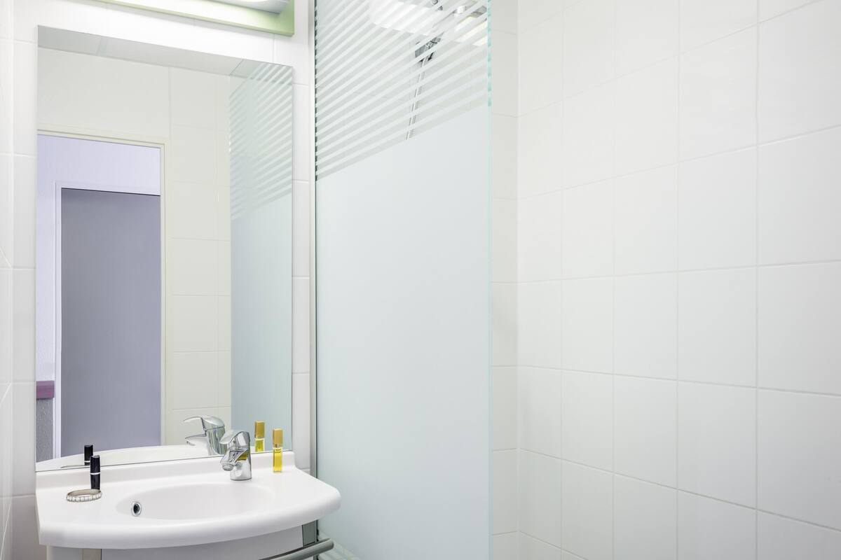 Baño con lavamanos, espejo y azulejos blancos.