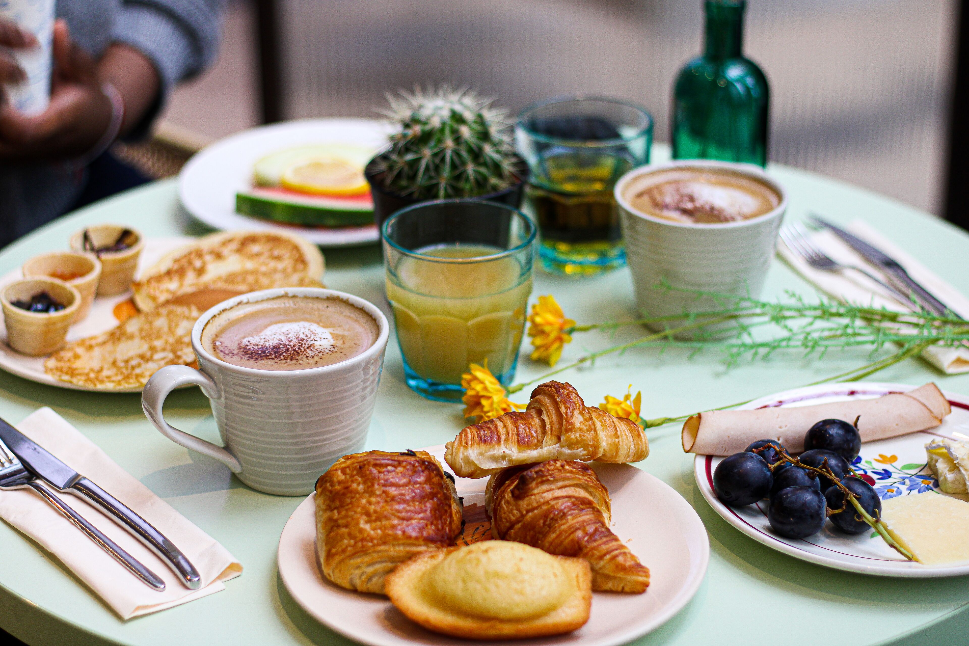 Mesa de pequeno-almoço com croissants, uma chávena de café e um prato de mirtilos.