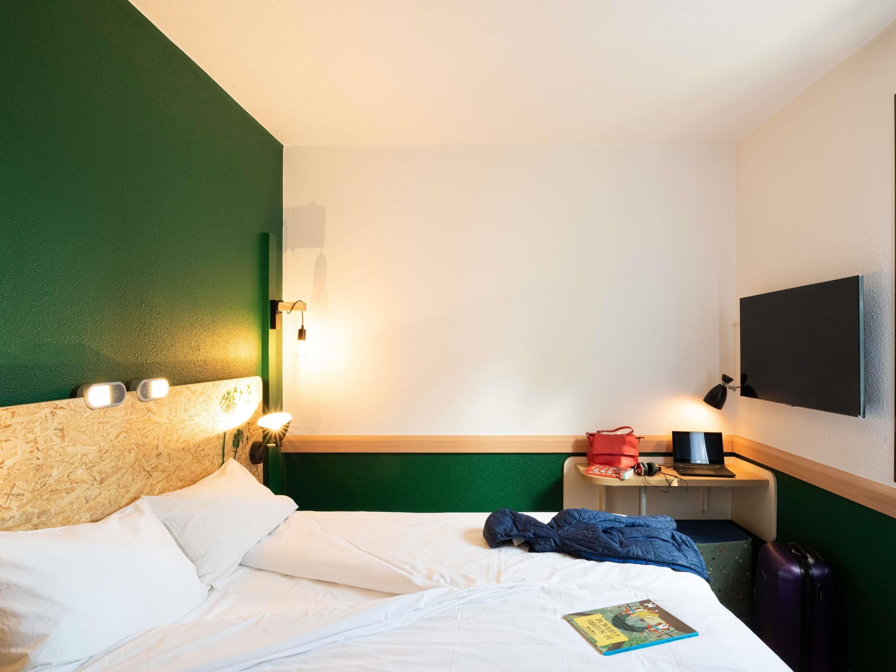 Une chambre d’hôtel avec un lit, un bureau avec un ordinateur portable, une télévision et une lampe de chevet.