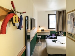 Habitación de hotel con cama, escritorio con computadora portátil, televisión, ventana con cortinas y un soporte de bicicleta en la pared con cascos.