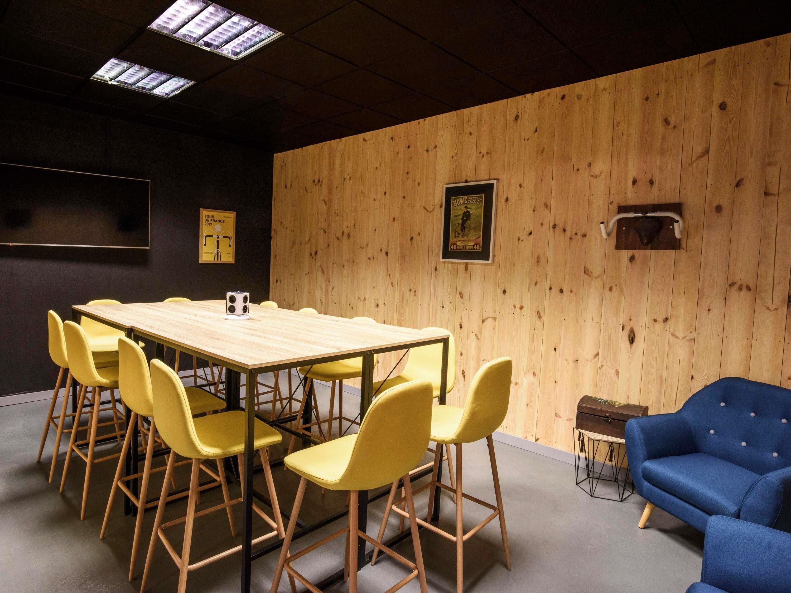 A conference room with a wooden table and yellow chairs, a blue sofa, and a poster on the wall.