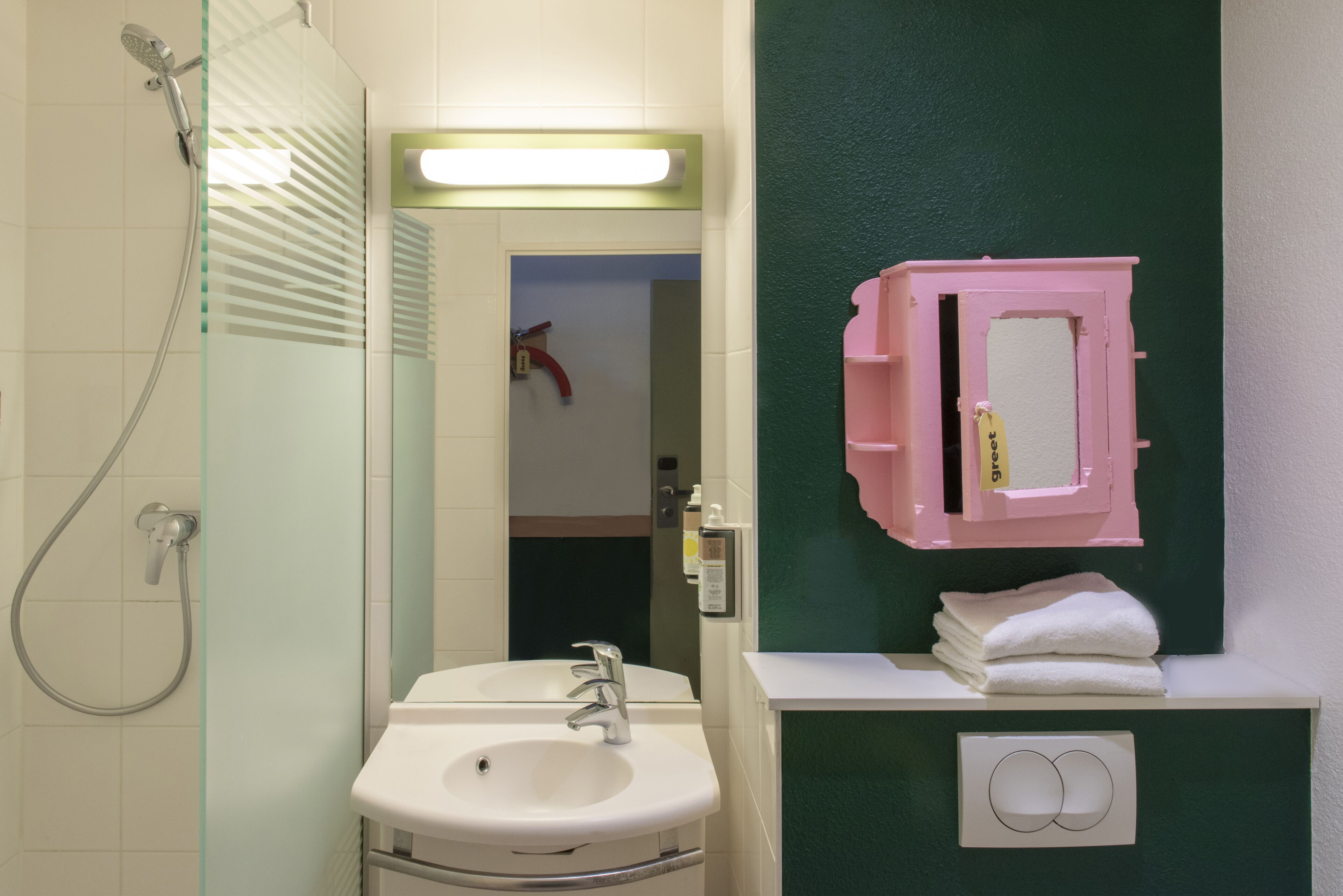 A bathroom with a glass shower enclosure, a white sink, and a mirror with a pink frame.
