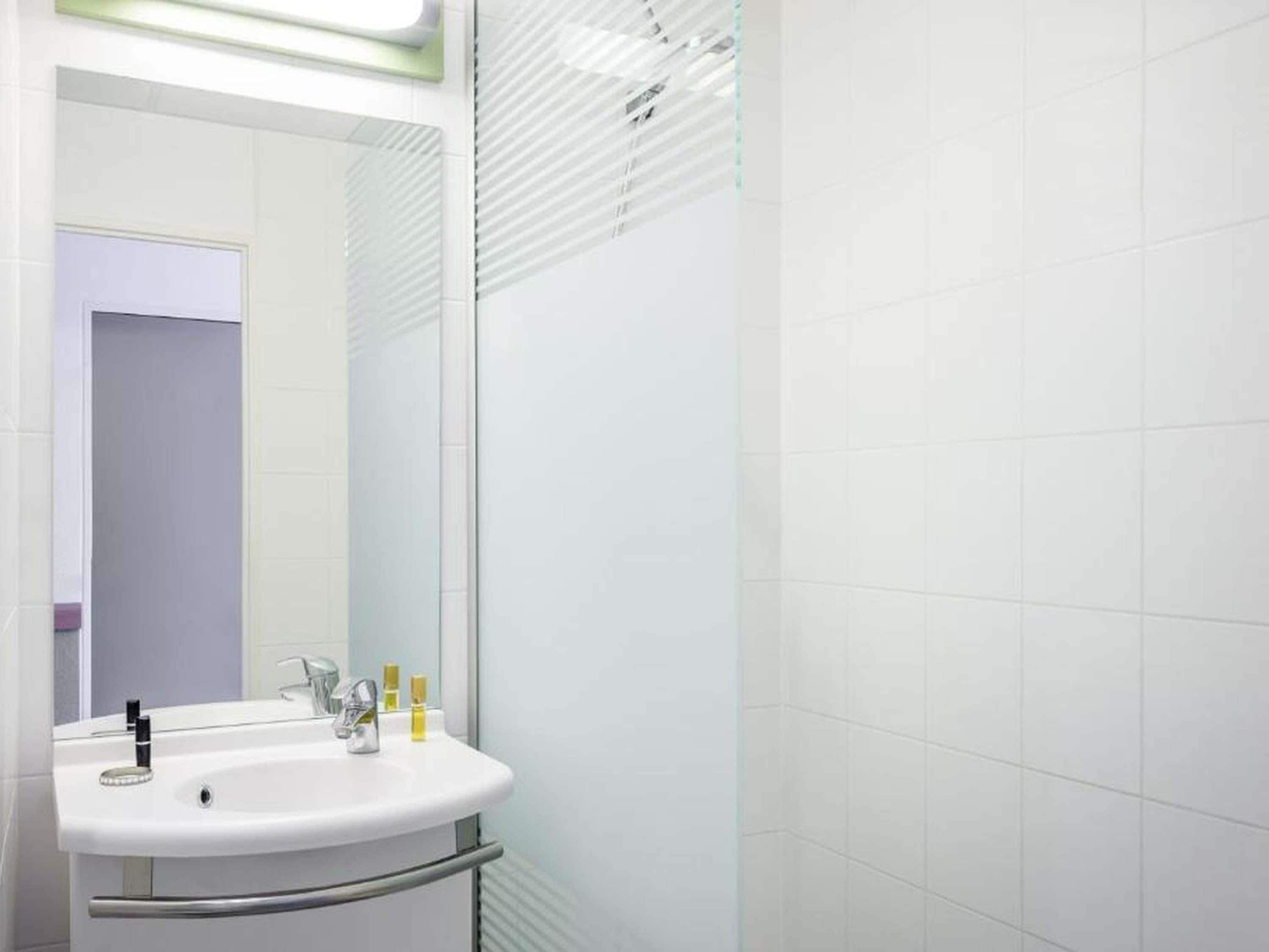 Un baño con lavamanos blanco, espejo y paredes con azulejos.