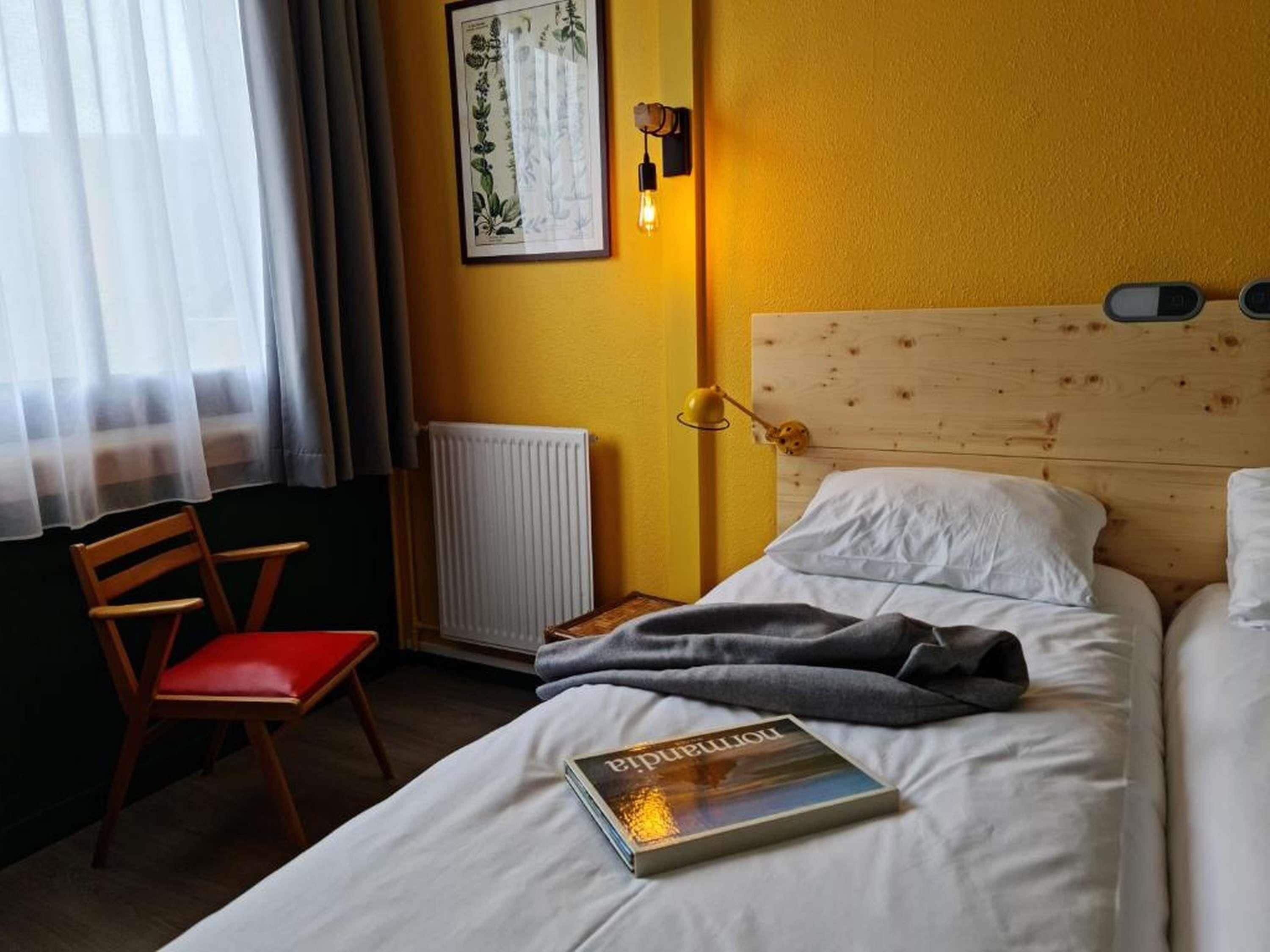 A hotel room with a single bed, a bedside table, a chair, a radiator, and a wall-mounted light fixture.