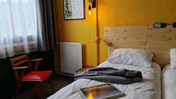 A hotel room with a single bed, a bedside table, a chair, a radiator, and a wall-mounted light fixture.