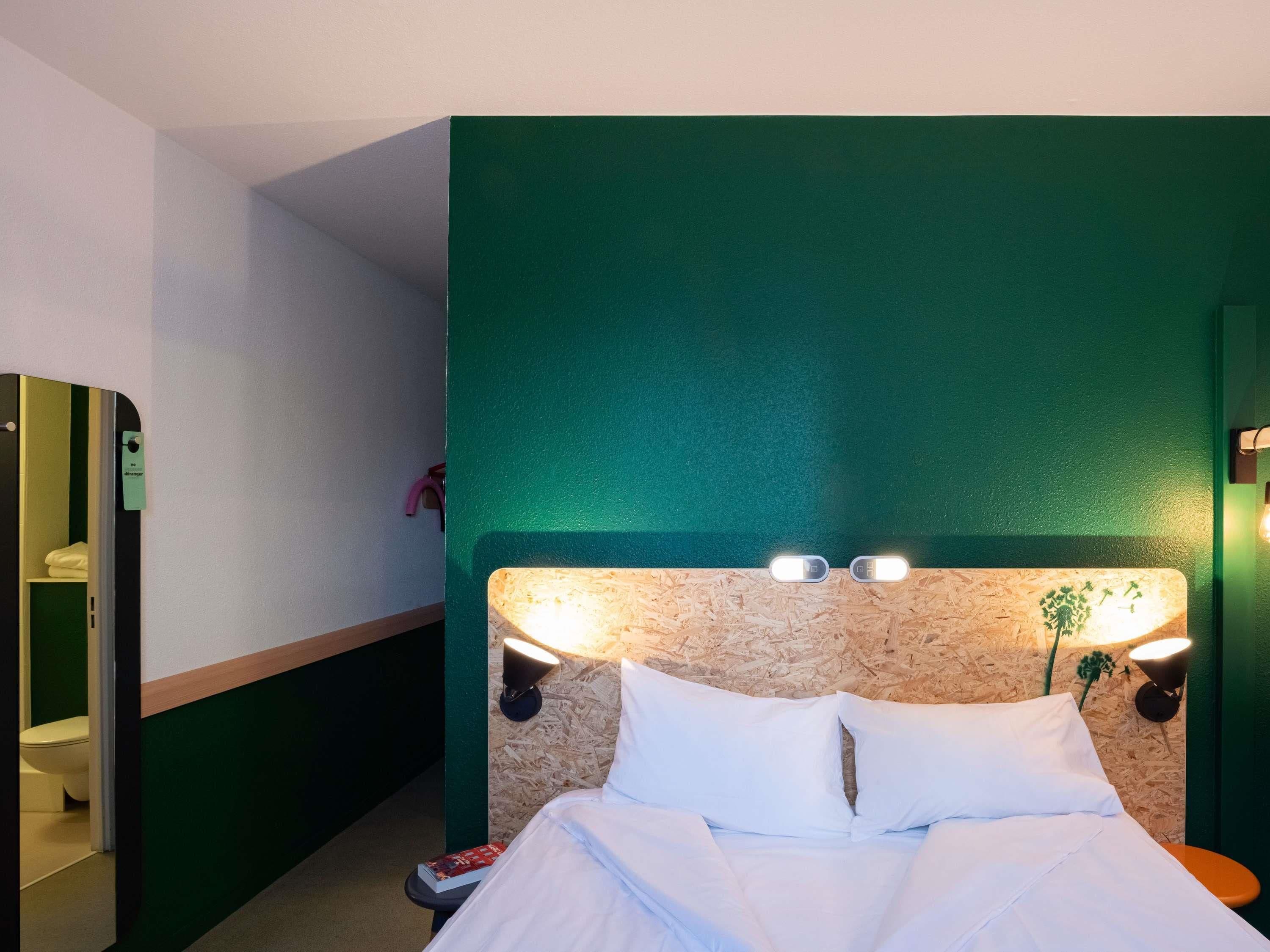 Et hotelværelse med en seng, et natbord, et spejl og en grøn accentvæg.