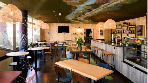 A restaurant interior with wooden walls, multiple tables and chairs, hanging lamps, and a bar area with bottles. - Greet Hotel Evreux Centre - Route de Normandie by Accor (Evreux)