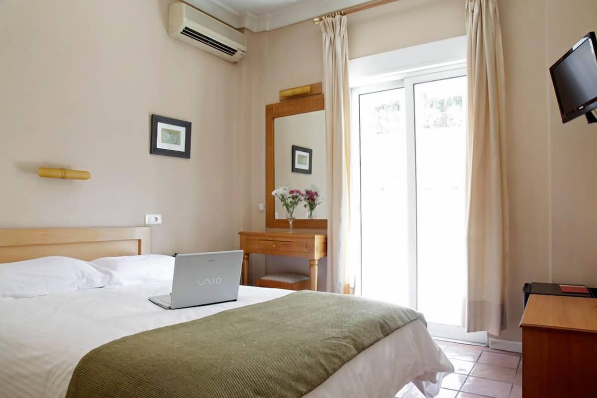 A hotel room with a bed, a desk with a laptop, a mirror, and a TV.