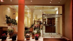 The entrance of Bella Hotel with a neon sign, potted plants, and a reception desk. - Pella (Thessaloniki)