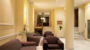 A hotel lobby with sofas, a coffee table, a staircase, and a plant. - Pella (Thessaloniki)