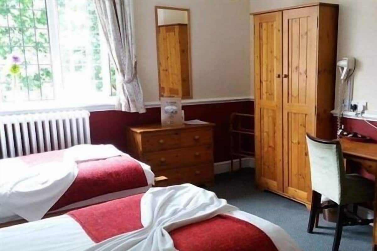A room with two beds, a wooden wardrobe, a desk, and a chair.
