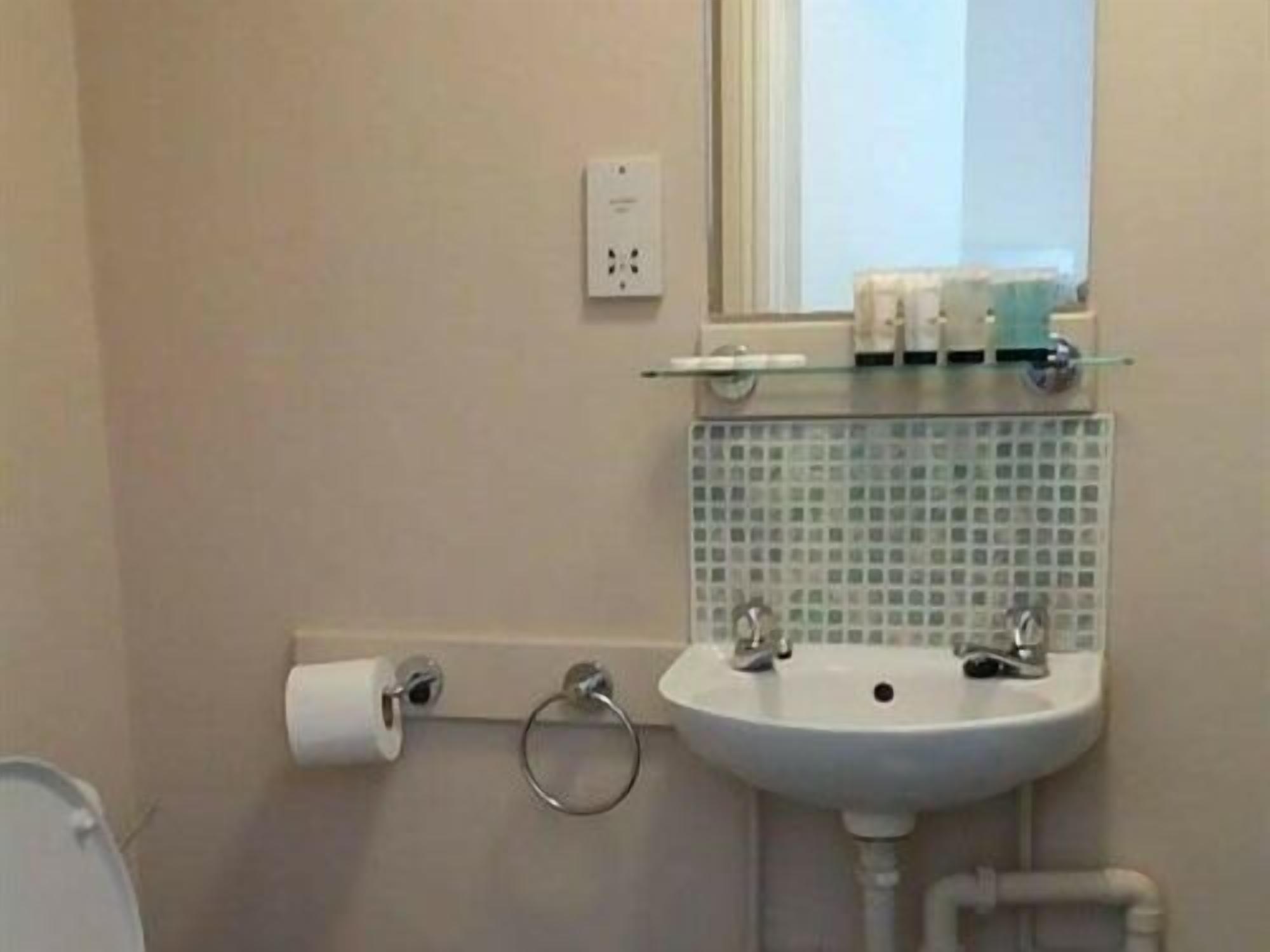 A bathroom with a white sink, a mirror, a toilet paper holder, and a glass shelf with toiletries.