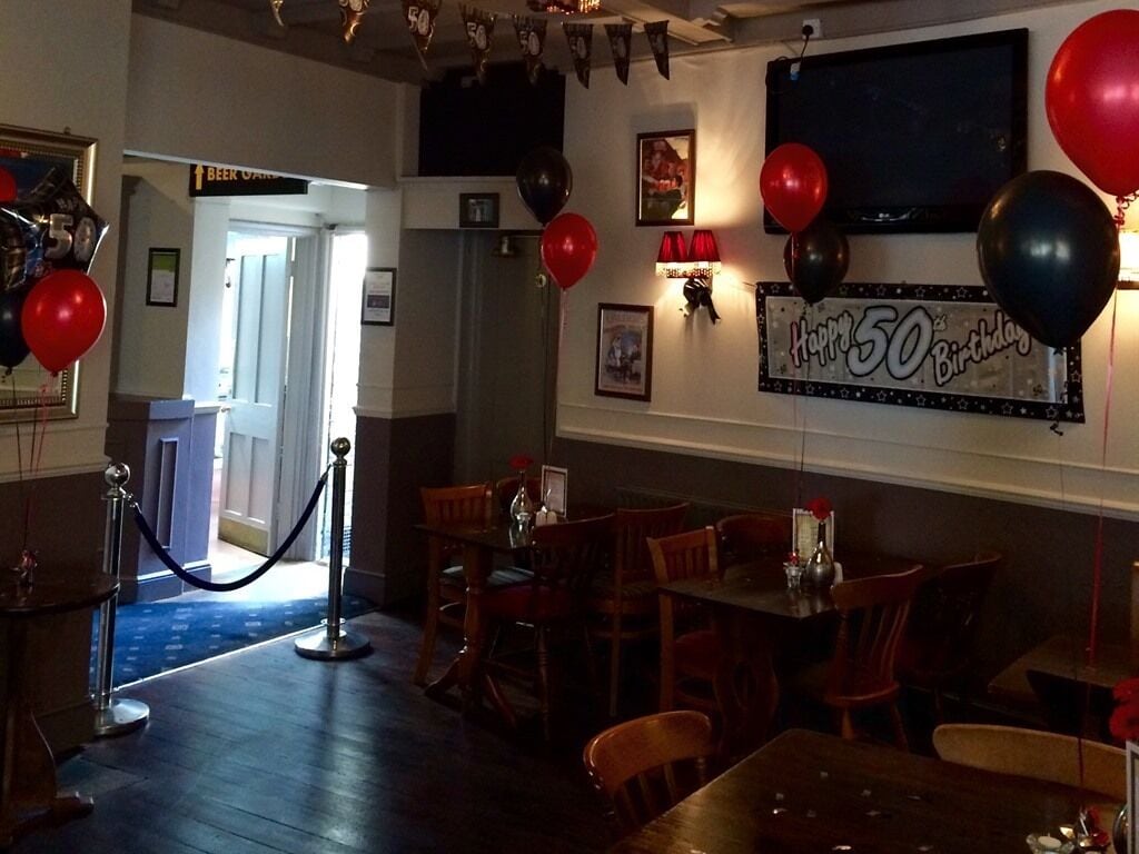 A restaurant interior with a '50th Birthday' celebration theme, featuring balloons, a 'Beer Garden' sign, and a 'Happy 50th Birthday' banner.