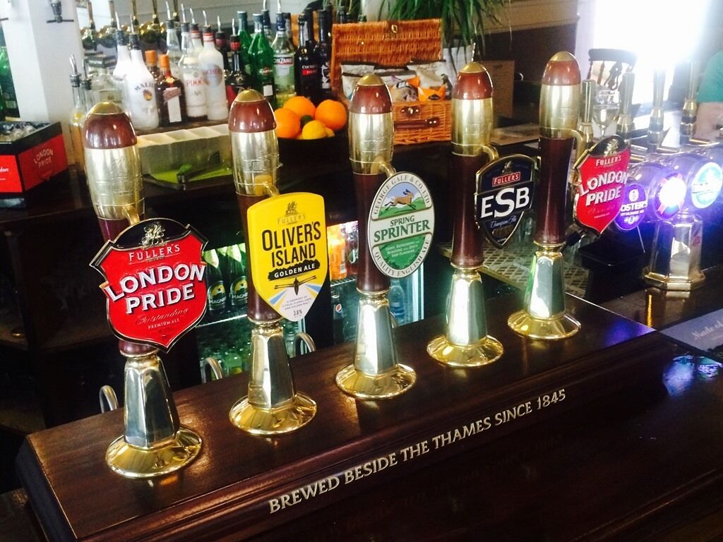 Um balcão de bar com diversas torneiras de cerveja, incluindo marcas como Fuller's London Pride e Olivers Island Gold.