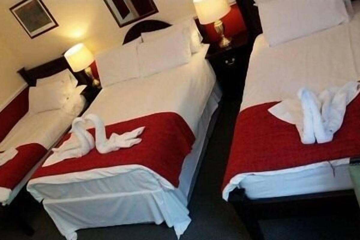 A hotel room with two beds, each with a red bedspread and white linens. There are two bedside tables with lamps.