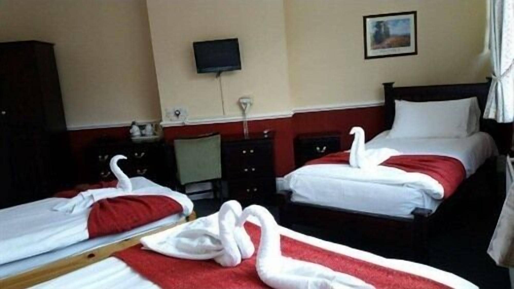 A hotel room with two beds, each with a red and white bedspread and a white swan decoration. There is a television on the wall and a small desk with a chair.