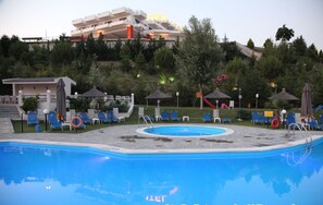 A swimming pool with lounge chairs and umbrellas, a hotel building in the background, and a hilly landscape. - Acropol (Serres)