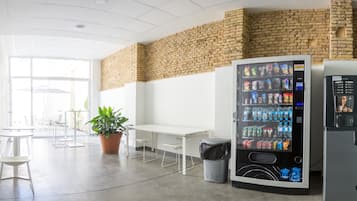 A modern indoor space with a brick wall, a vending machine, a trash bin, and a potted plant.