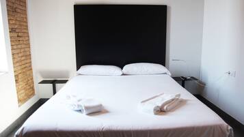 Una habitación de hotel con una cama grande, cabecera negra, ropa de cama blanca y una pared de ladrillo.