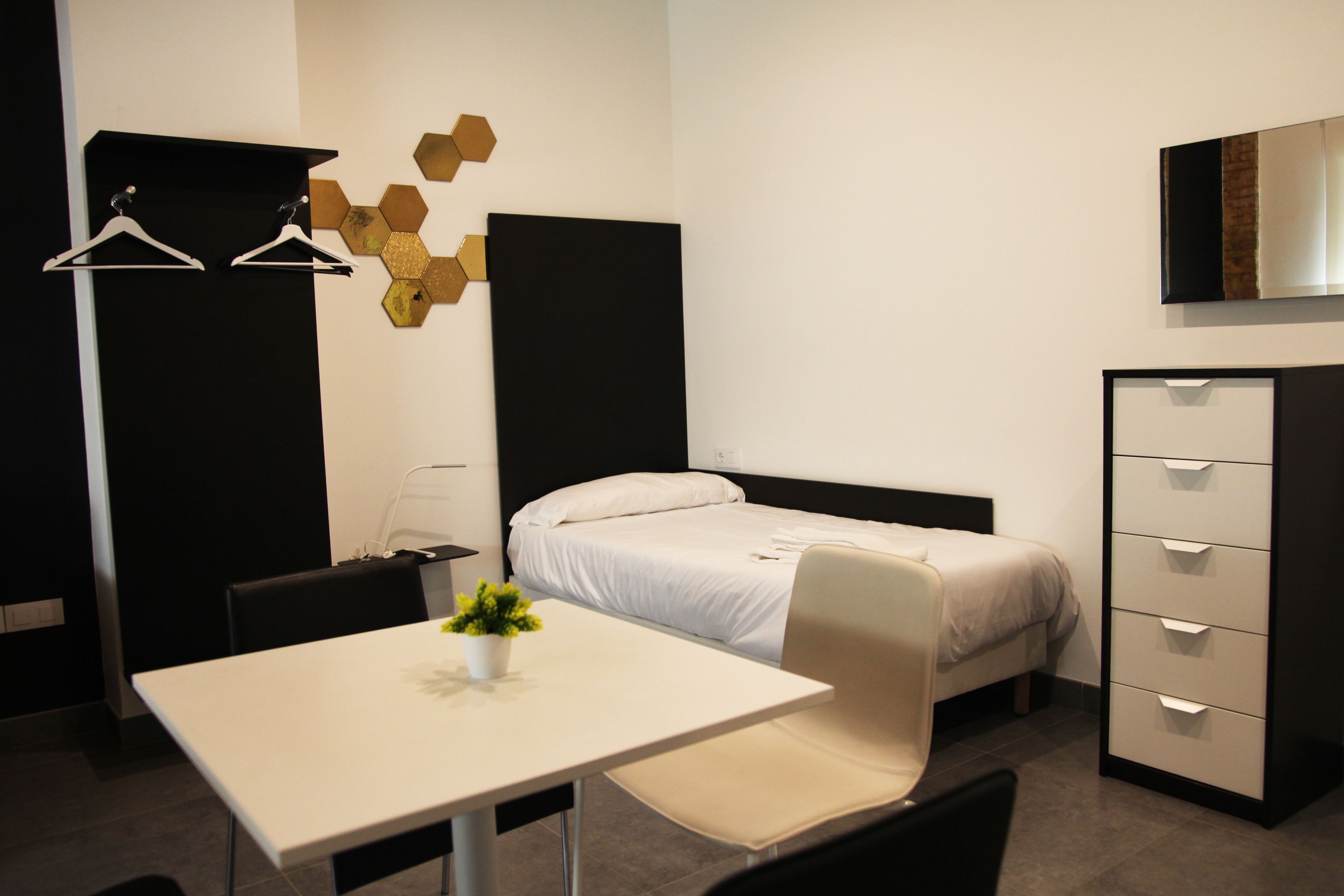A hotel room with a bed, a desk, a chair, a dresser, and a wall-mounted TV.