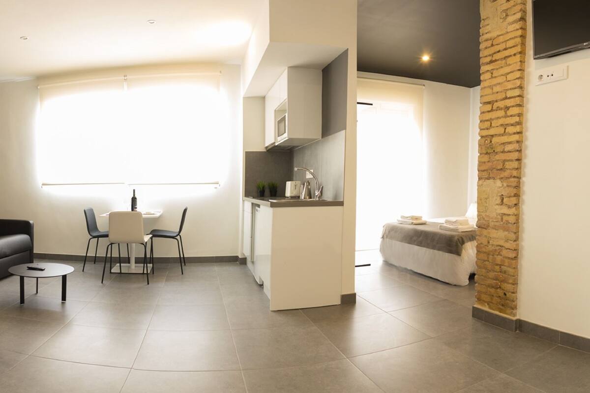 Habitación de hotel compacta con cama, sofá, pequeña mesa de comedor y kitchenette.