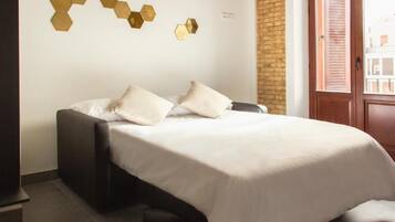 A neatly made bed with white bedding and two pillows, a wall-mounted hexagonal light fixture, and a brick wall.